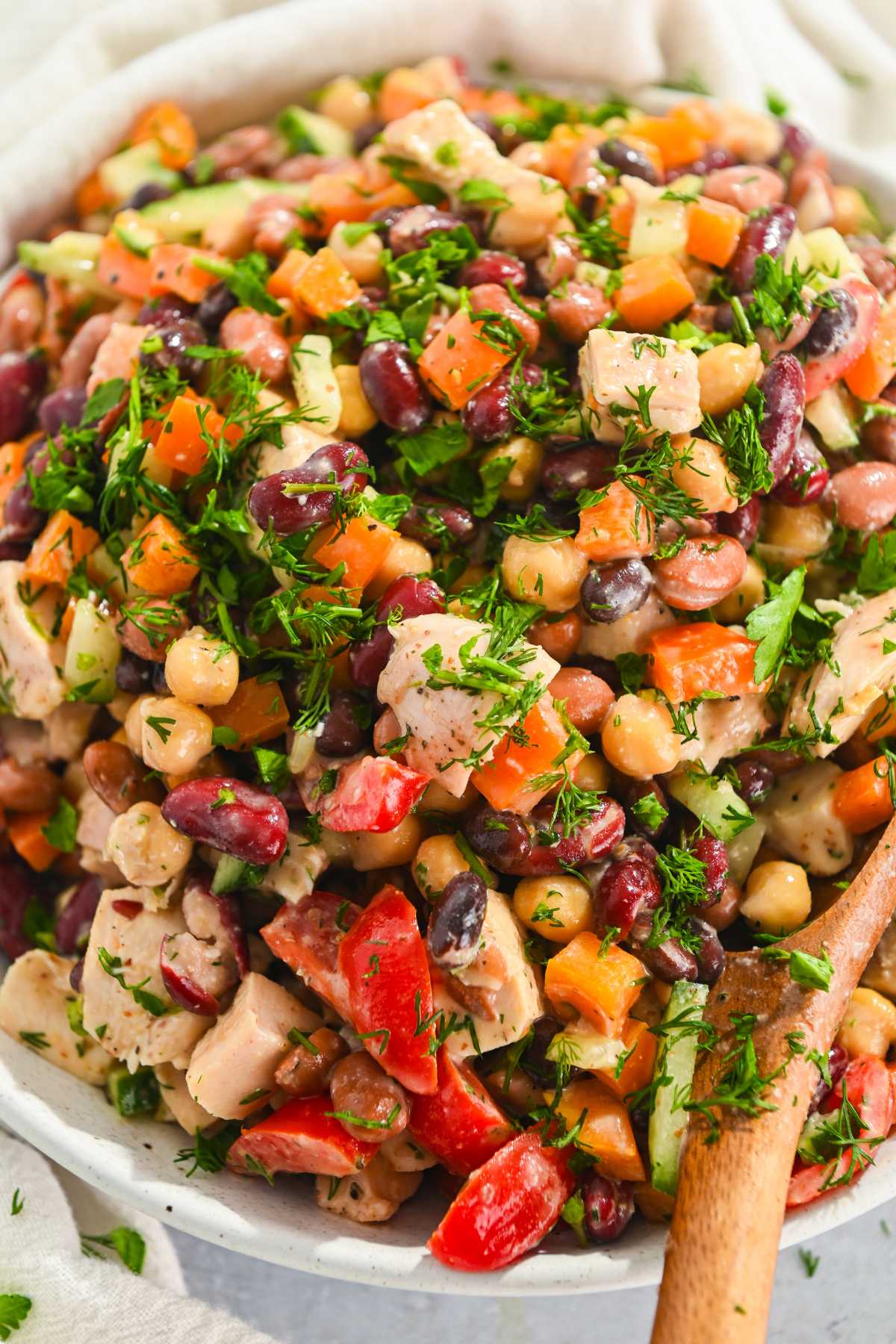 close up of dense bean salad with chicken in a white bowl with fresh herbs on top.