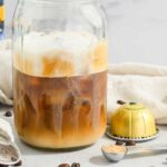 close up of Nespresso coffee in a mason jar with foam on top and with capsules, brown sugar, and coffee beans around it.