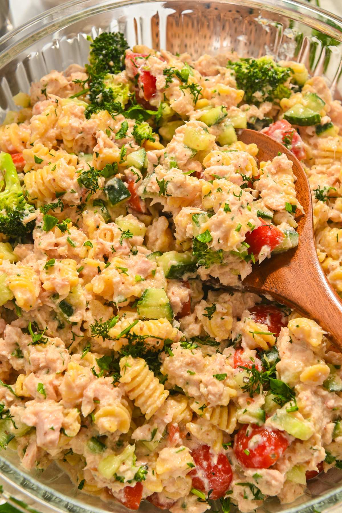 close up of high protein tuna pasta salad in a glass bowl with a wooden spoon.