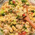 close up of high protein tuna pasta salad in a glass bowl with a wooden spoon.