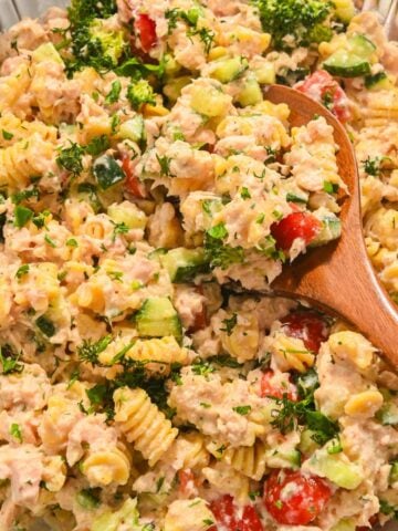 close up of high protein tuna pasta salad in a glass bowl with a wooden spoon.
