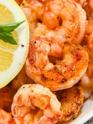 zoomed in photo of Blackstone griddle shrimp topped with seasonings, next to a lemon.