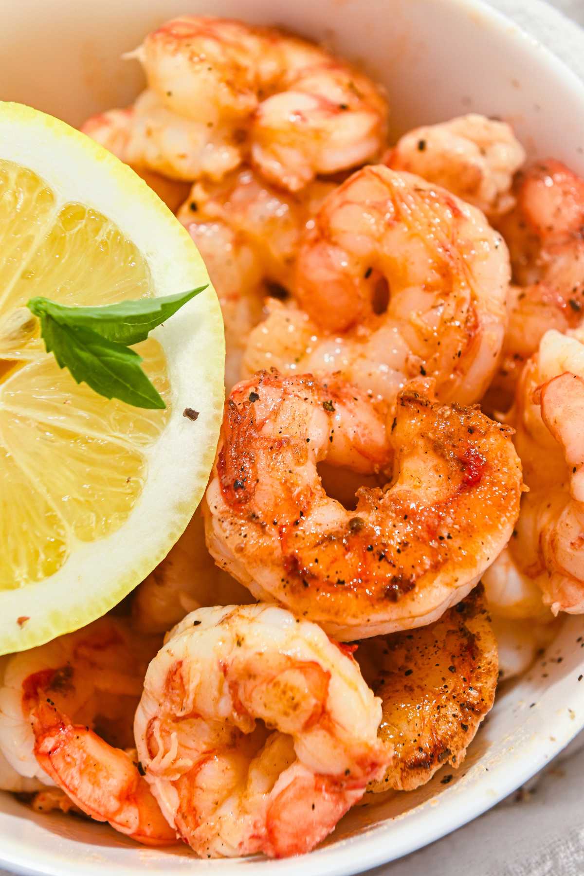close up of cooked blackstone shrimp topped with pepper and garnished with lemon and basil.