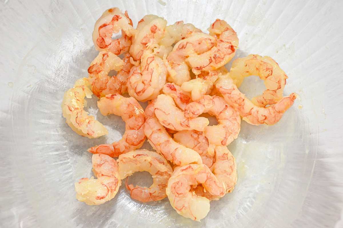 raw shrimp in a glass bowl on a gray background.