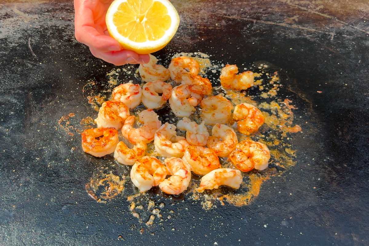 cooked garlic butter shrimp on the blackstone griddle being seasoned with lemon.