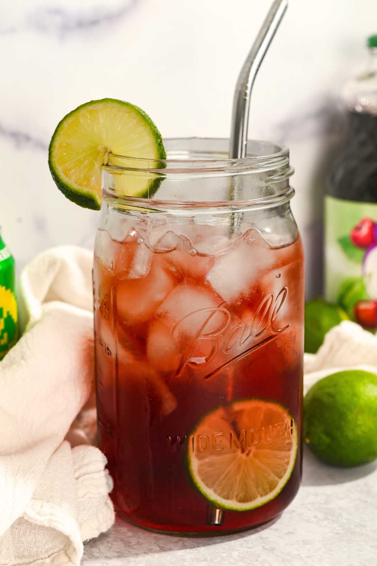 Iced tart cherry mocktail in a glass mason jar with a lime for garnish and served with a stainless steel straw.