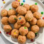 cropped top down view of no-bake monster protein balls with m&ms on a white plate.