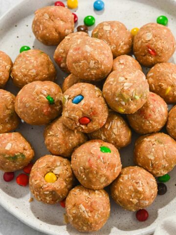 cropped top down view of no-bake monster protein balls with m&ms on a white plate.