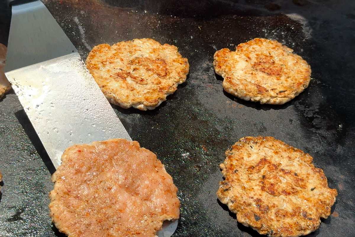 smash turkey burgers on a griddle with a spatula under one.