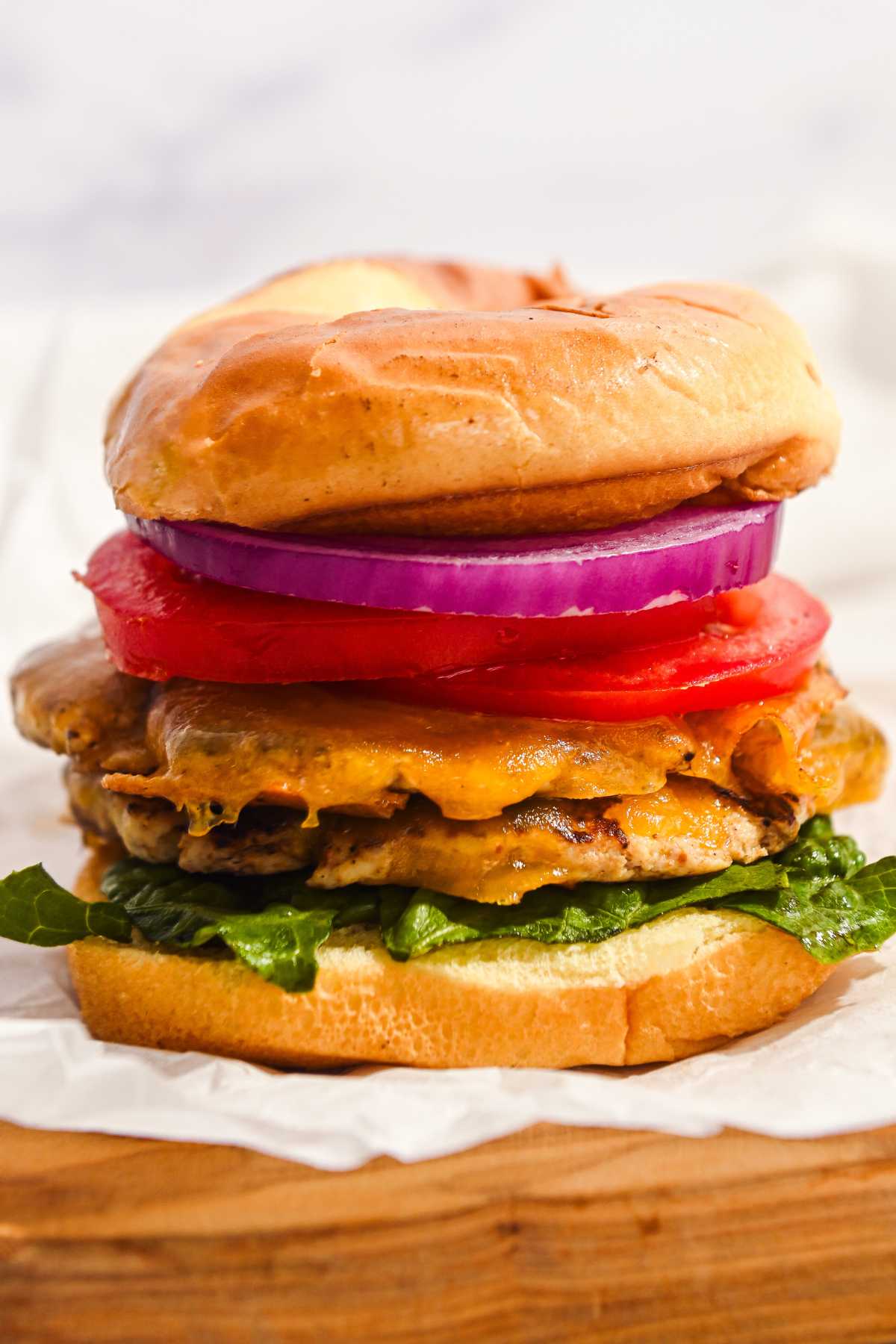 close up of a turkey smash burger on a bun with lettuce, cheese, tomato, and onion.