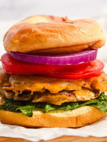 stacked turkey smash burger with cheddar cheese, lettuce, tomato, and onion on a bun.