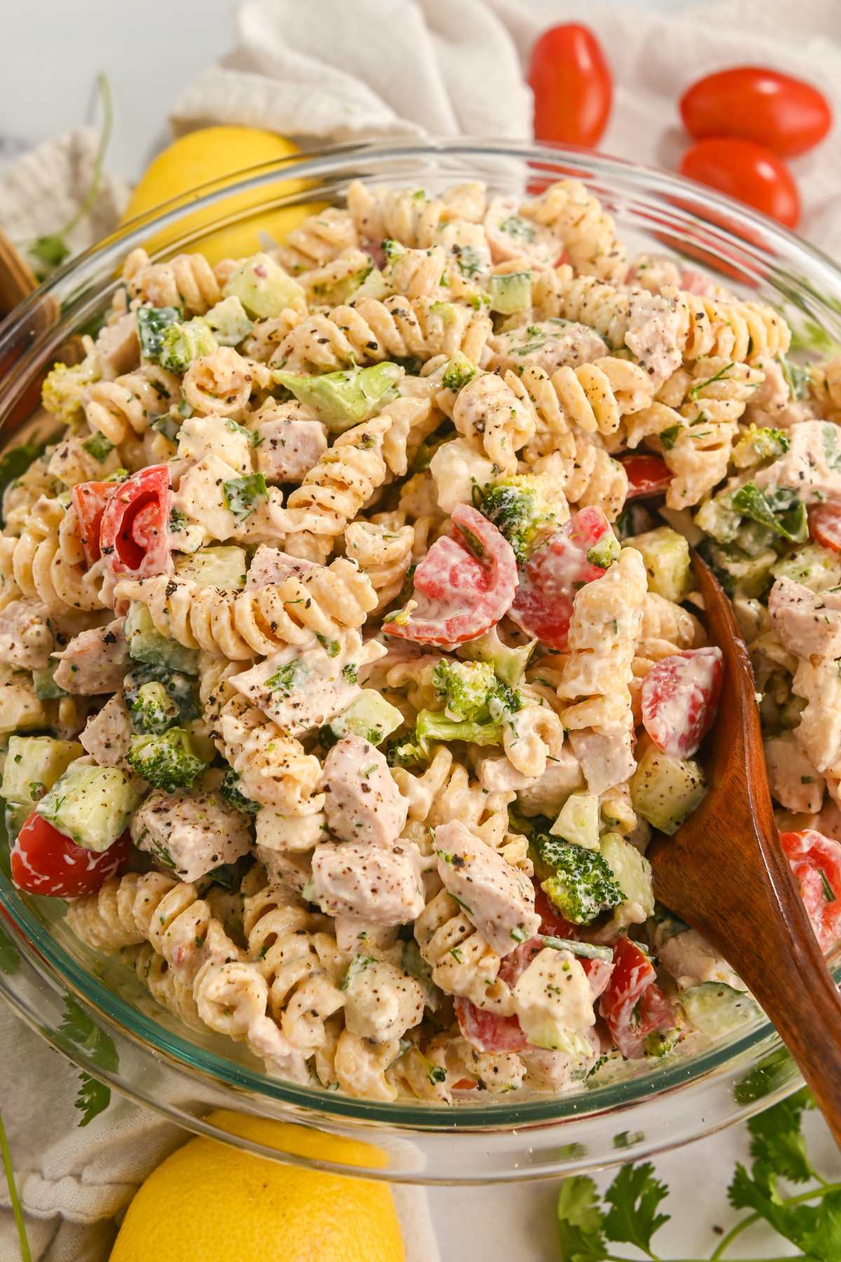 overhead view of creamy protein pasta salad with chicken and vegetables in a glass bowl with a wooden spoon.