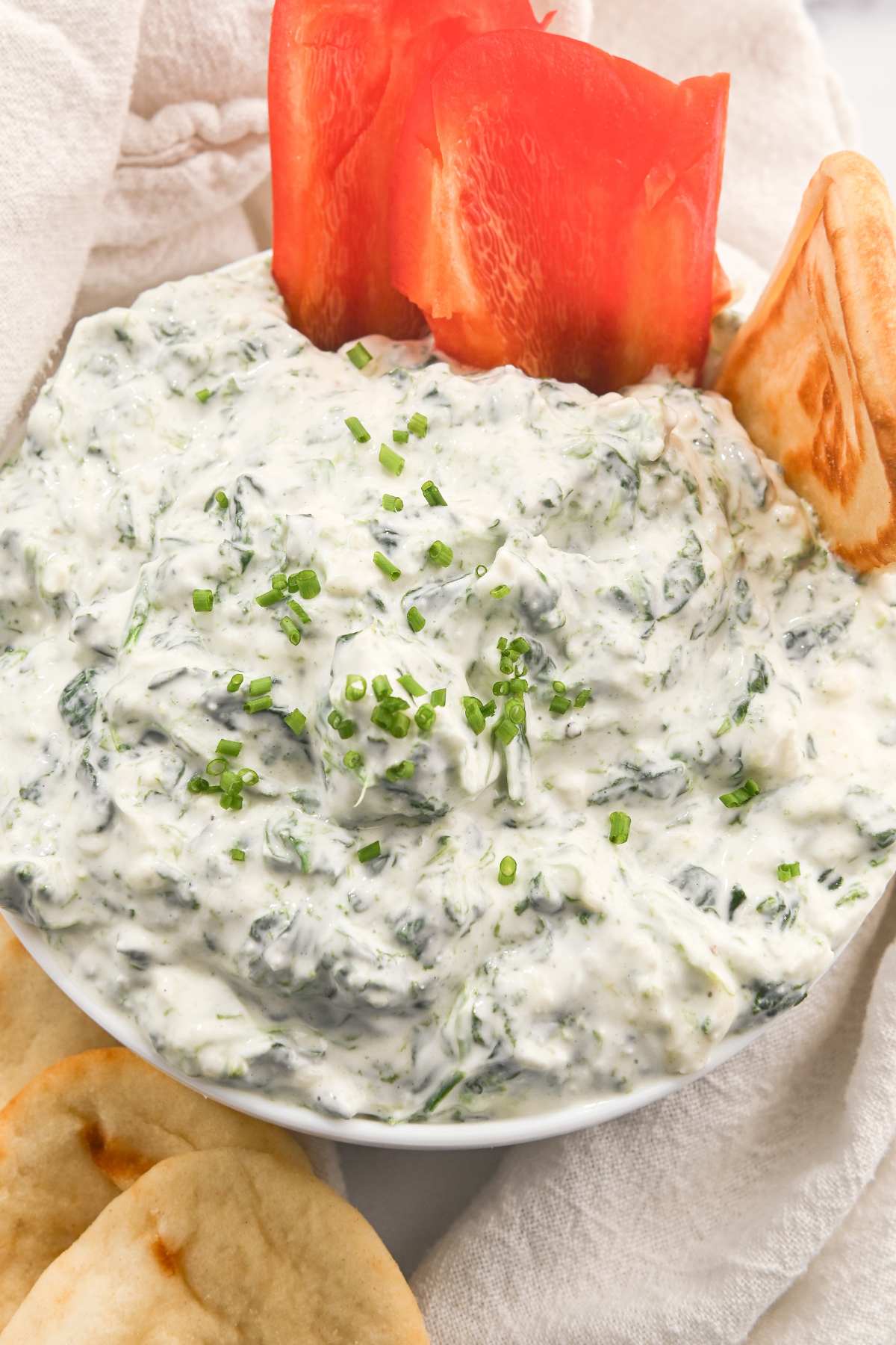 overhead view of high-protein spinach dip in a white bowl with peppers and pitas.