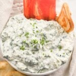 overhead view of cottage cheese spinach dip in a white bowl with peppers and pita bread.