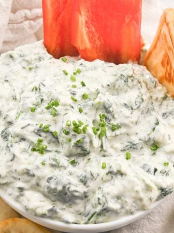 overhead view of cottage cheese spinach dip in a white bowl with peppers and pita bread.