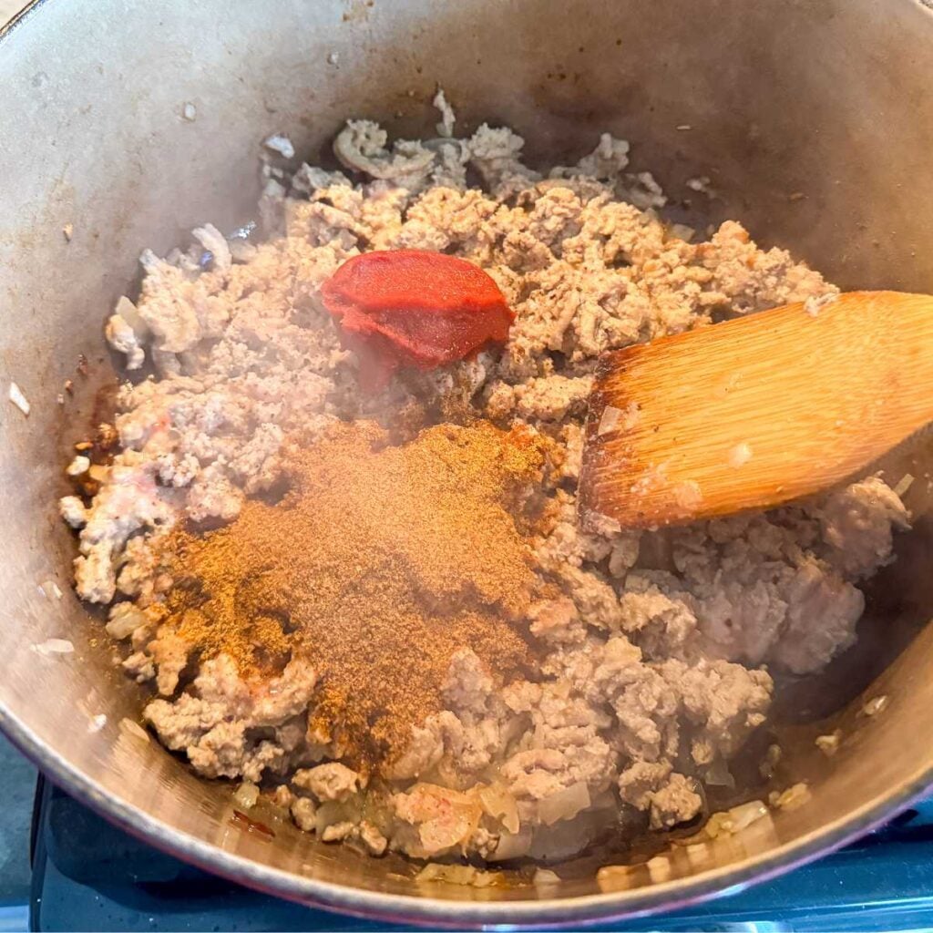 cooked ground turkey, seasoning, and tomato paste in a pot with a wooden spoon.