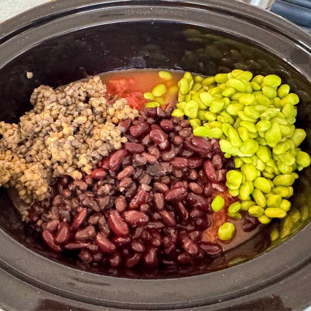 beans, lentils, and edamame in a crock pot with red liquid.