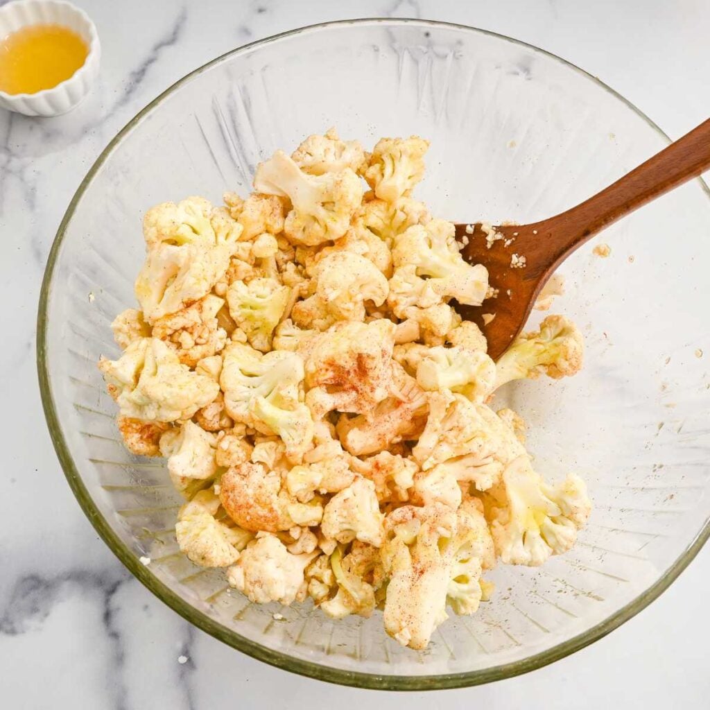 raw cauliflower with seasonings in a glass bowl.