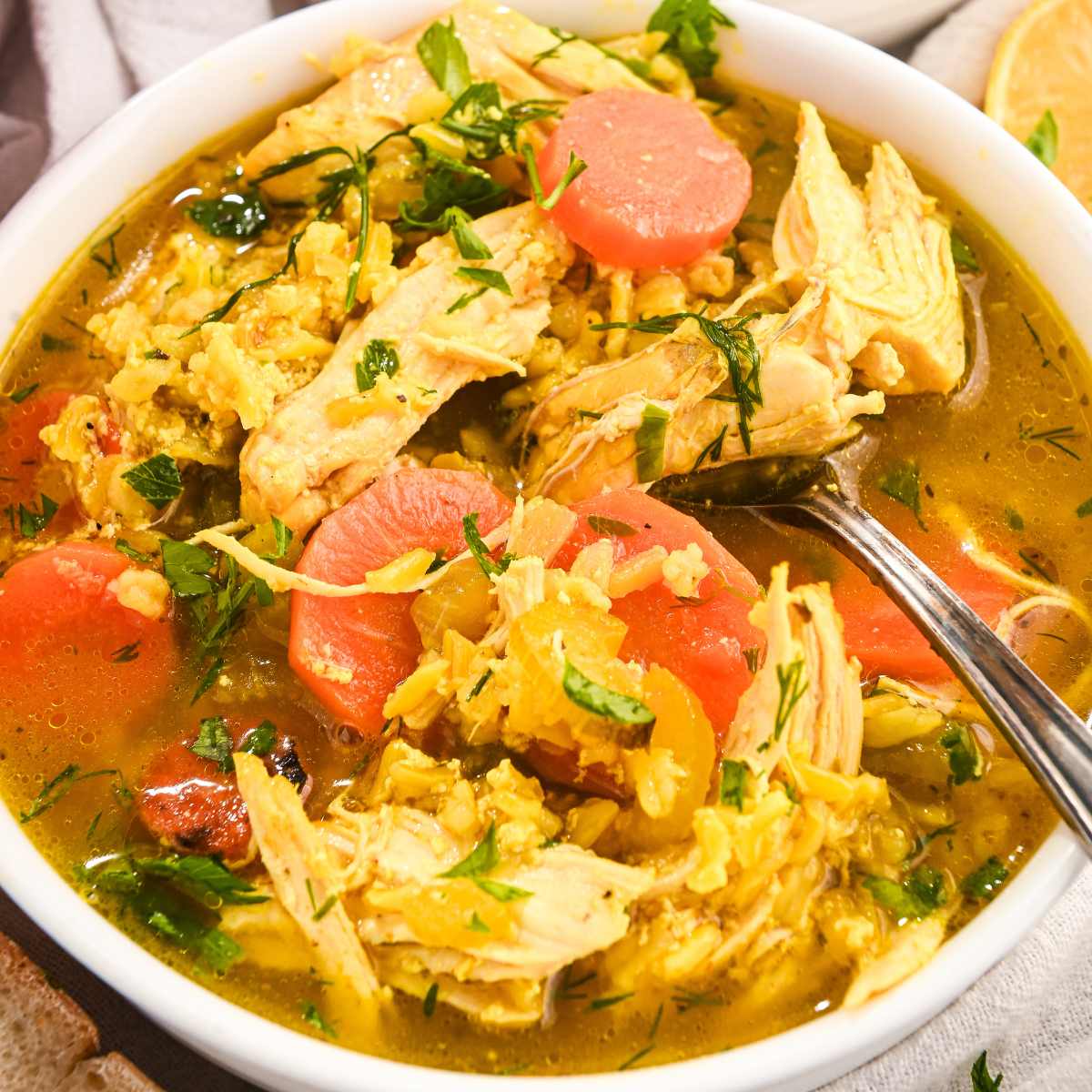 close up of lemon and turmeric chicken and rice soup topped with fresh herbs with a silver spoon.