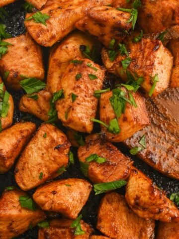 close up of hot honey chicken bites on a black air fryer tray with a wooden spatula.
