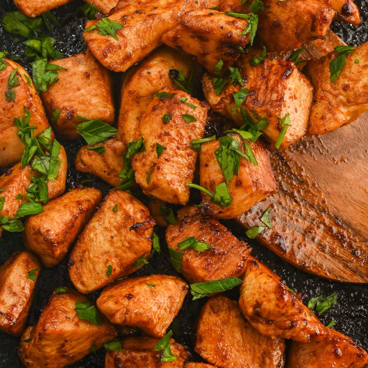 close up of hot honey chicken bites on a black air fryer tray with a wooden spatula.