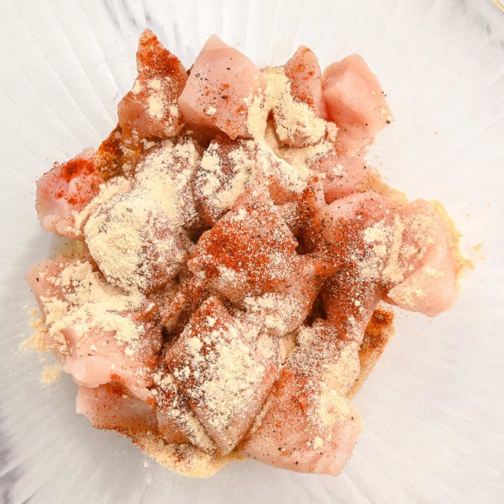 raw chicken covered with seasonings in a glass bowl.