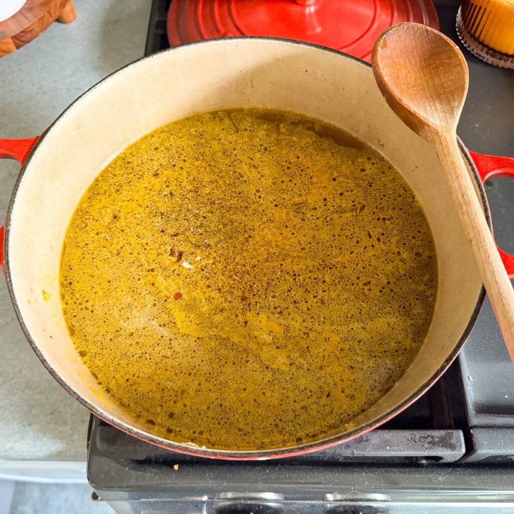 chicken broth in a Dutch oven with a wooden spoon.