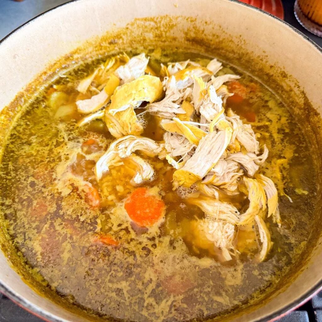 shredded chicken in chicken broth with carrots in a Dutch oven.