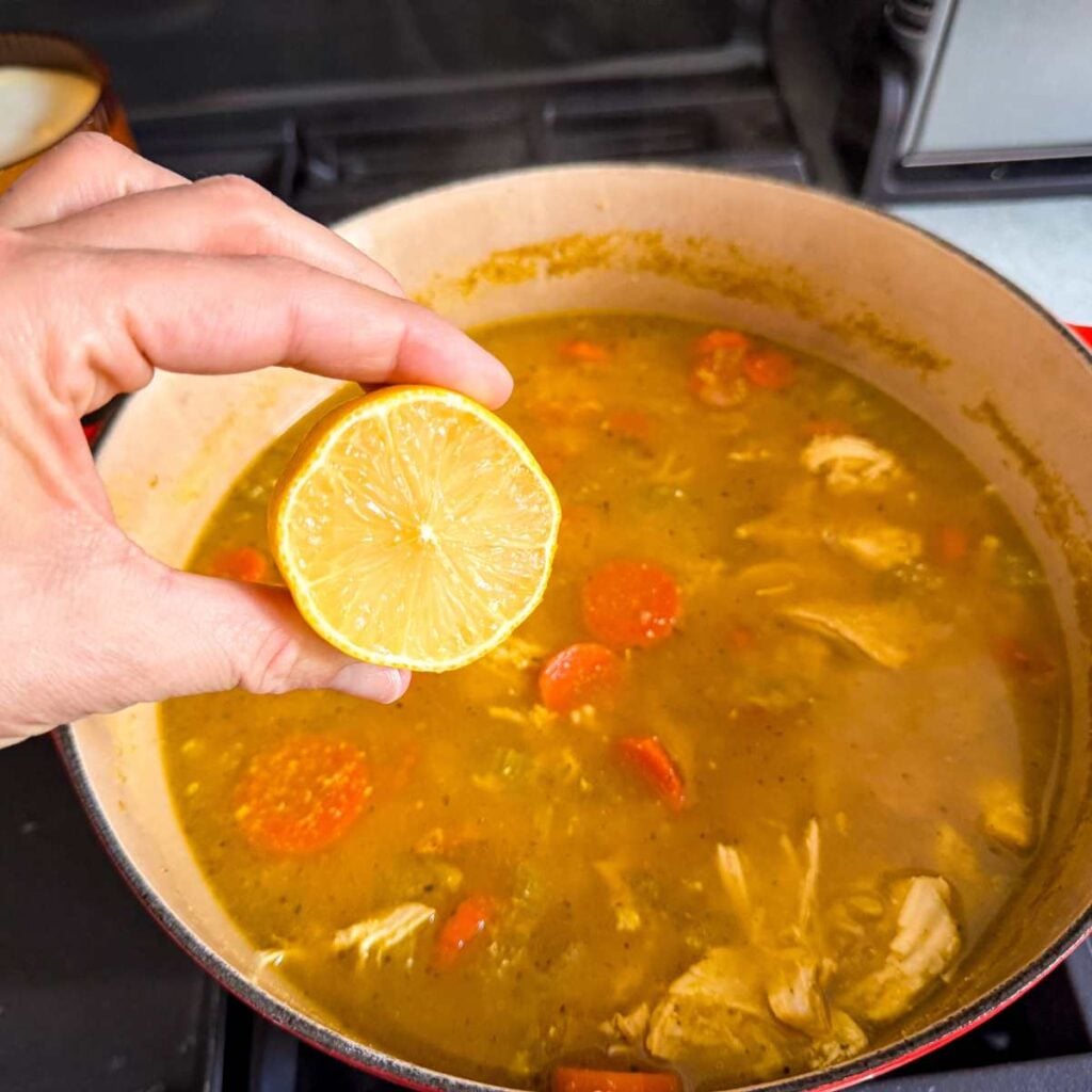 hand holding lemon above chicken and brown rice soup in a Dutch oven.
