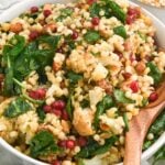 close up of winter roasted cauliflower salad in a white bowl with a wooden spoon.