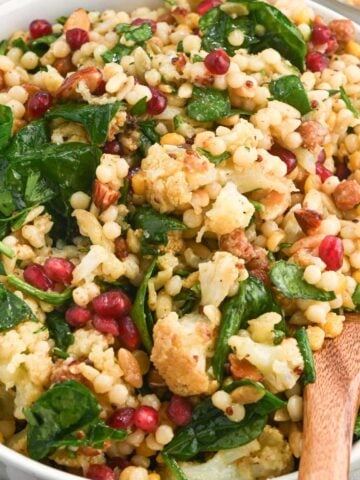 close up of winter roasted cauliflower salad in a white bowl with a wooden spoon.