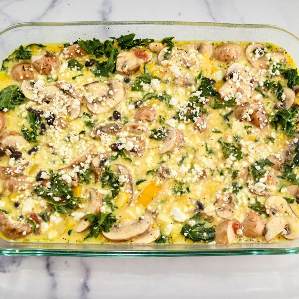 veggies and raw eggs in a flass dish ready for baking.