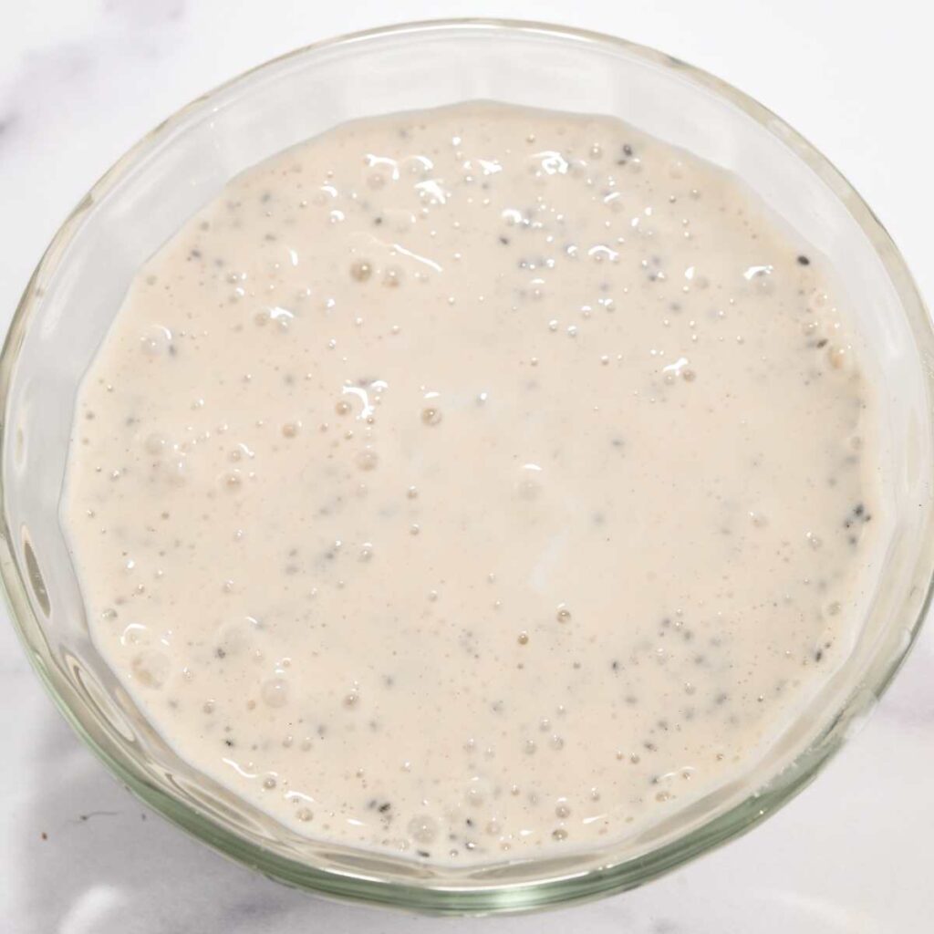 prepped cottage cheese chia pudding in a glass bowl on a white background.