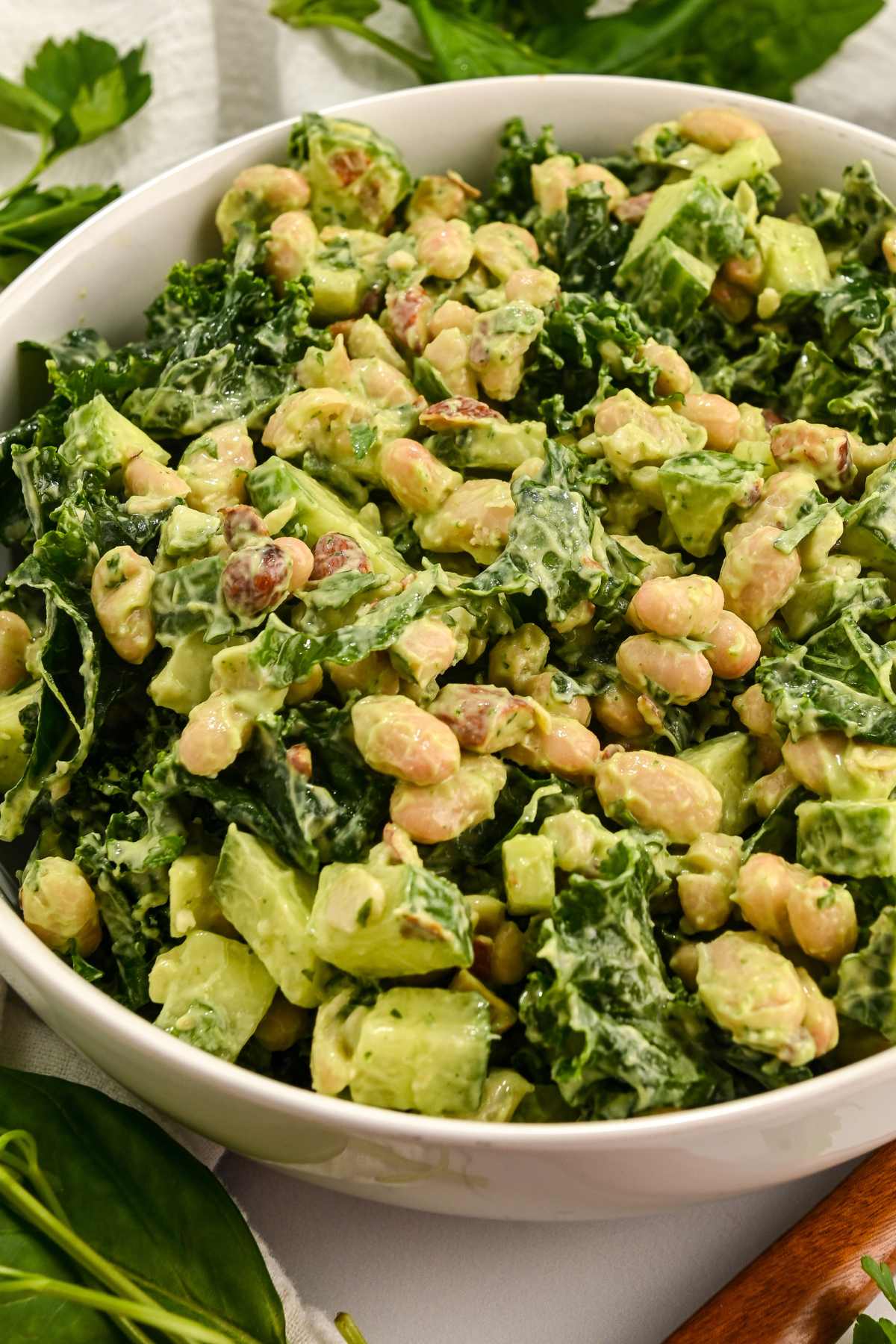 close up of green power salad in a white bowl with a wooden spoon.