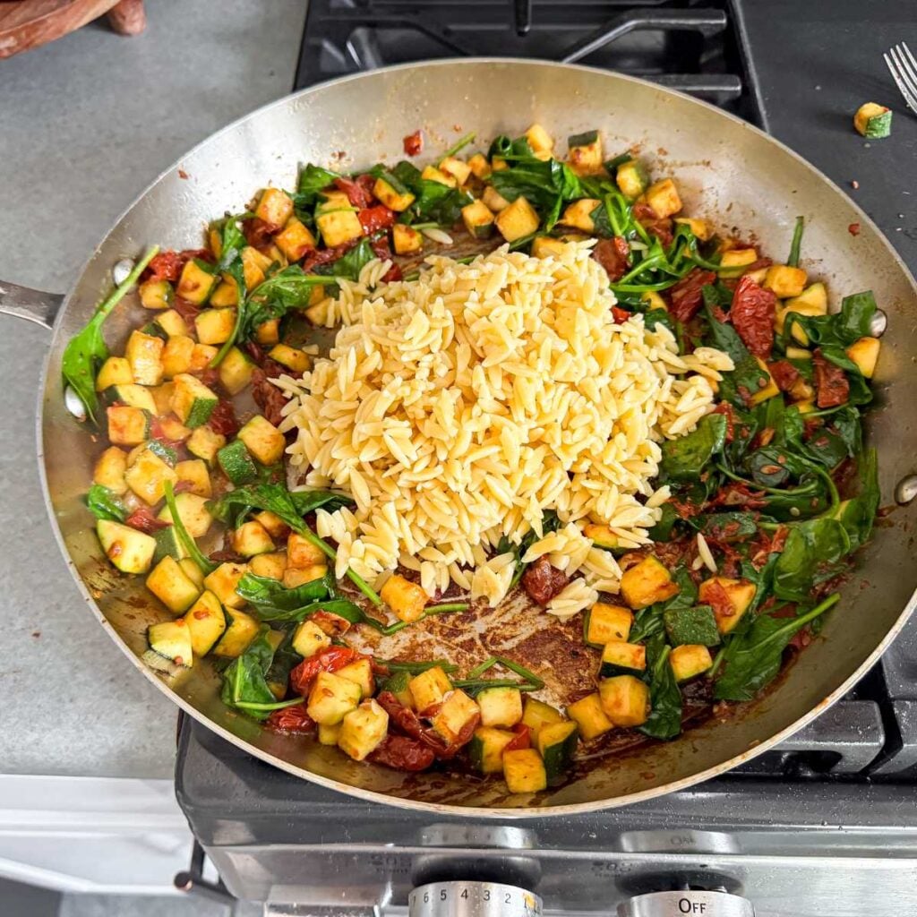 combined ingredients for creamy orzo with chicken in a skillet.