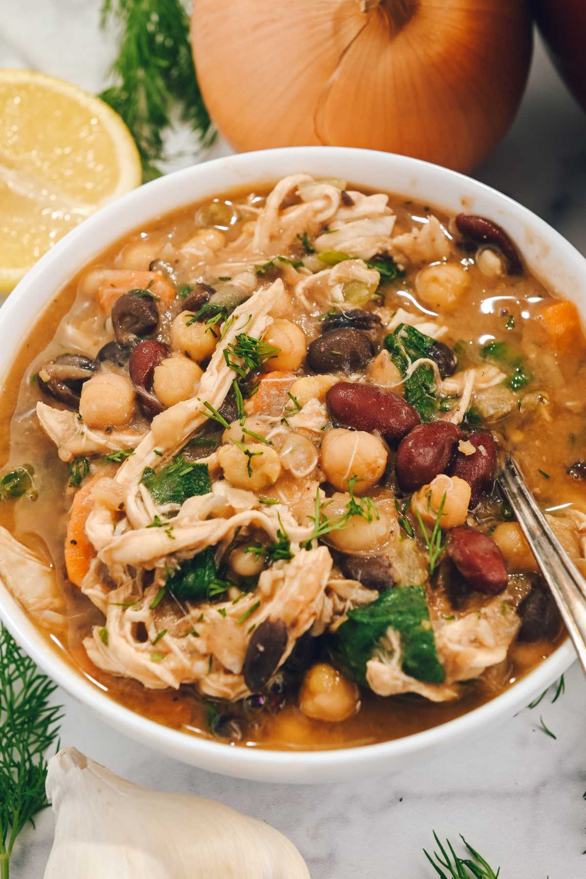 bean soup with chicken in a white bowl with a spoon and soup ingredients.