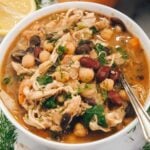 close up of bean soup with chicken in a white bowl with a spoon.