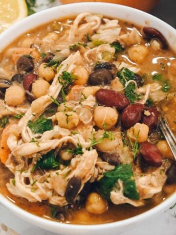 close up of bean soup with chicken in a white bowl with a spoon.