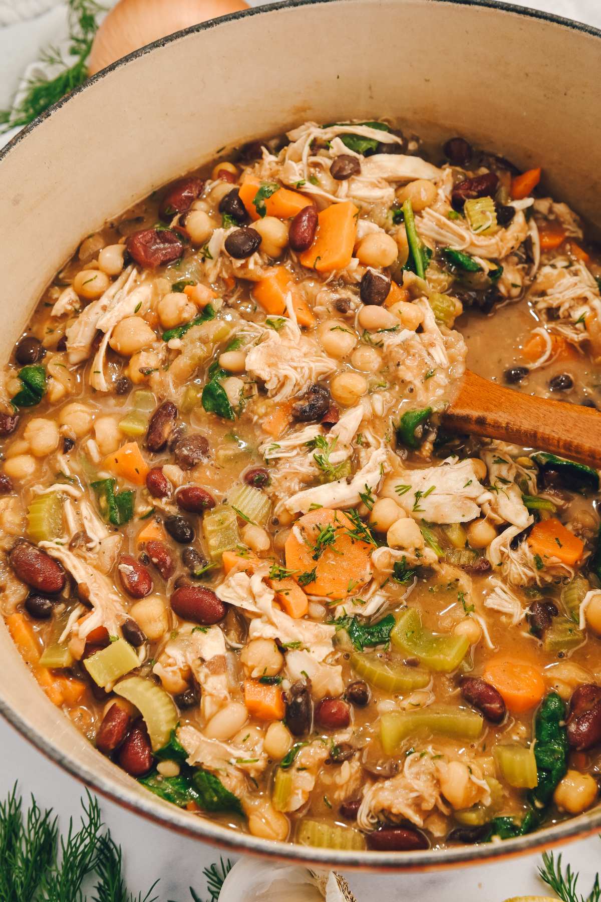 bean soup with chicken in a large soup pot with a wooden spoon.