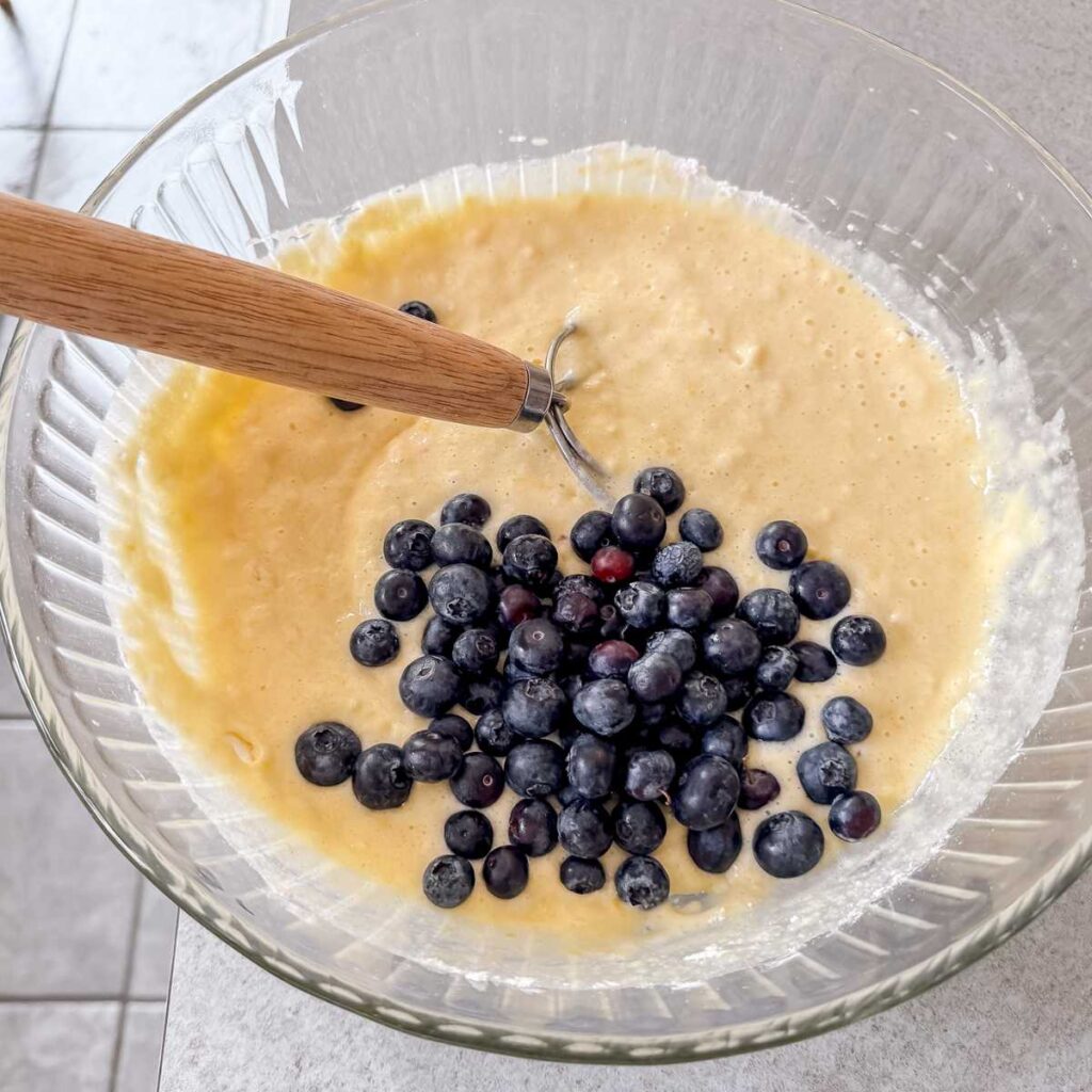 fresh blueberries being folded into lemon blueberry cake batter with a dough whisk.