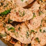 close up of creamy orzo with chicken in a skillet with a wooden spatula, topped with basil.