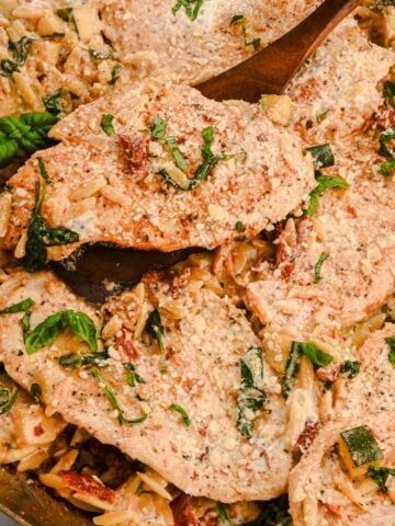 close up of creamy orzo with chicken in a skillet with a wooden spatula, topped with basil.
