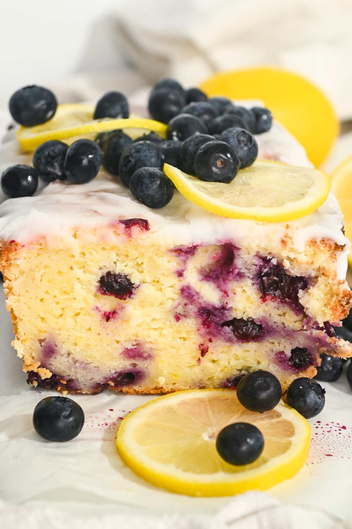 close up of greek yogurt blueberry lemon cake topped with fresh blueberries, lemons, and sugar free glaze.
