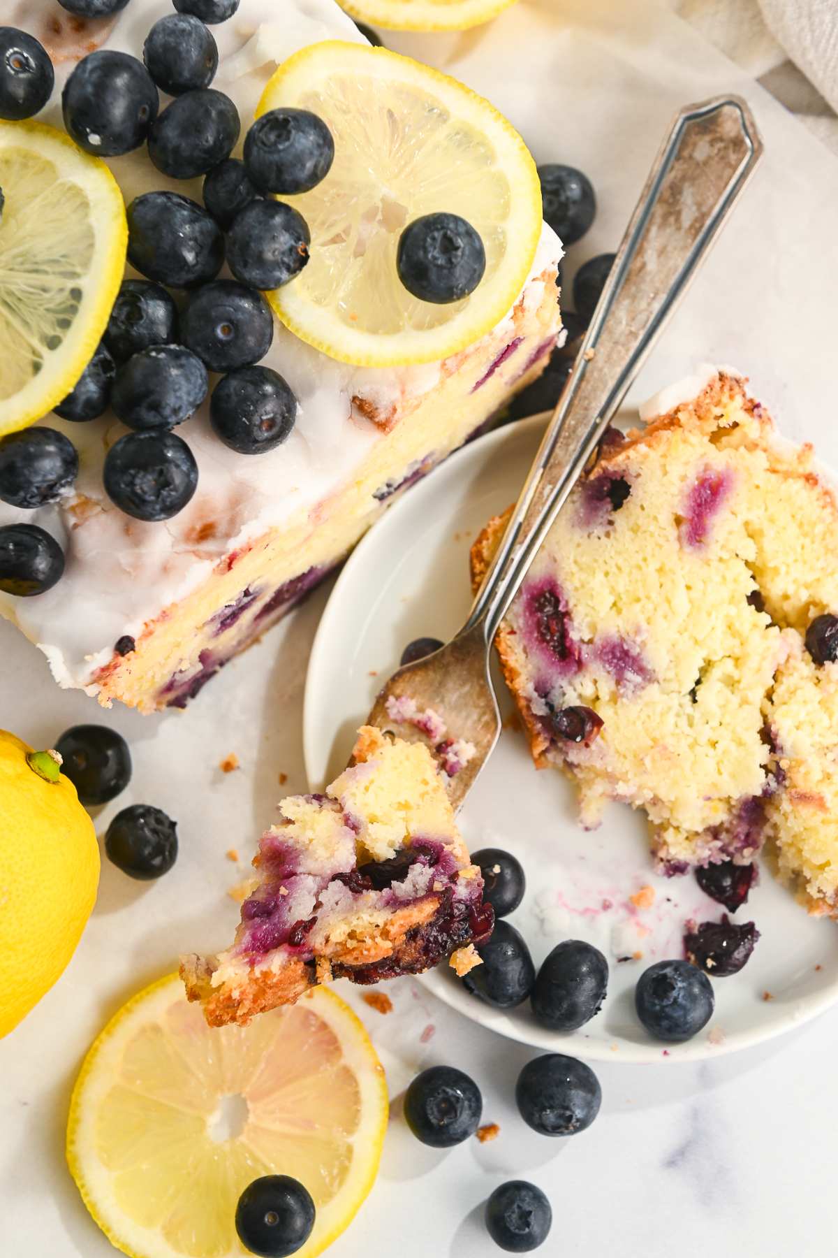 slice of greek yogurt lemon blueberry cake on a white plate with a fork.
