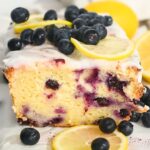 close up of greek yogurt lemon blueberry cake sliced open and topped with glaze.
