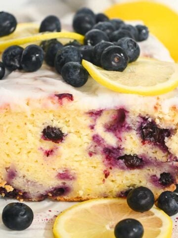 close up of greek yogurt lemon blueberry cake sliced open and topped with glaze.