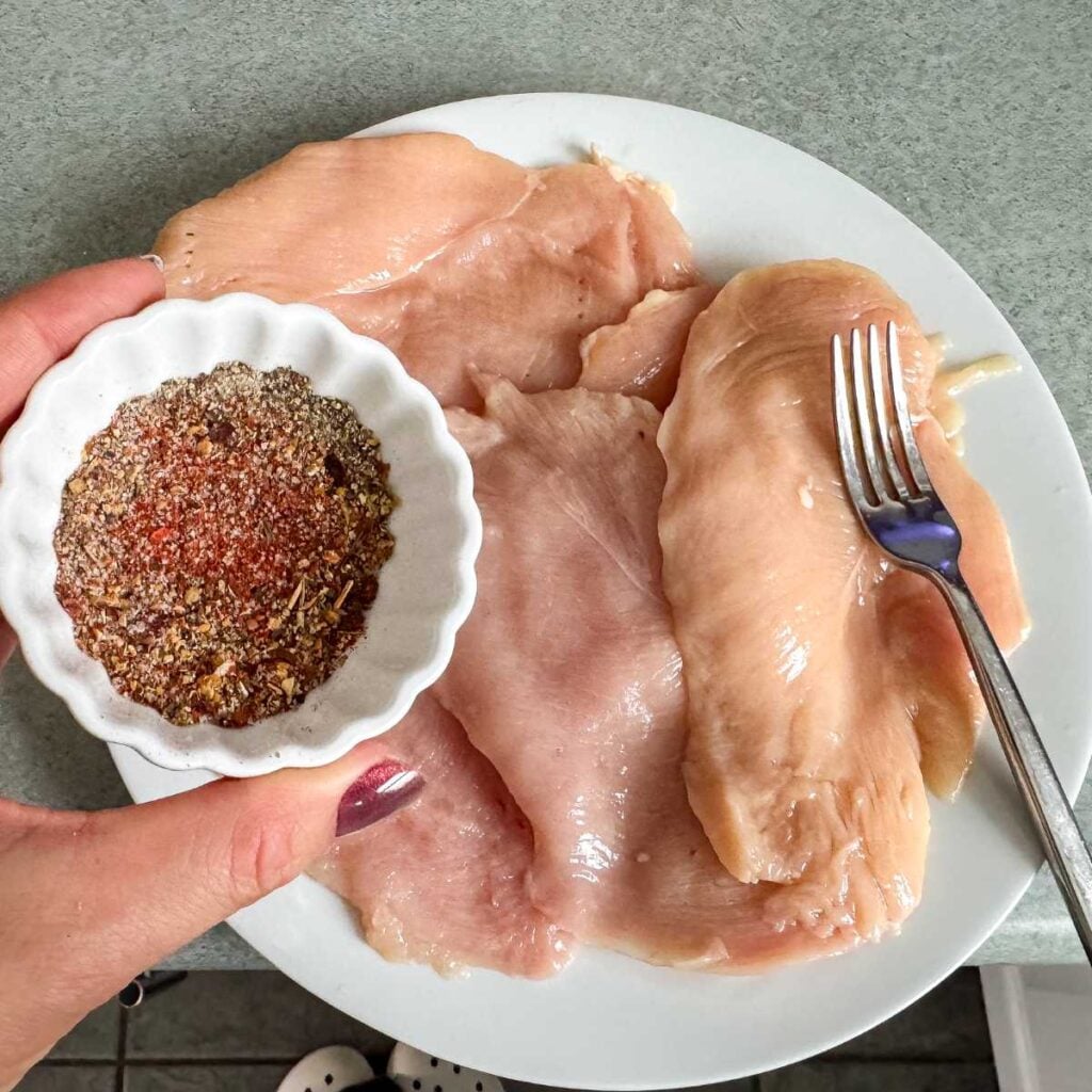 seasoning raw chicken breast.
