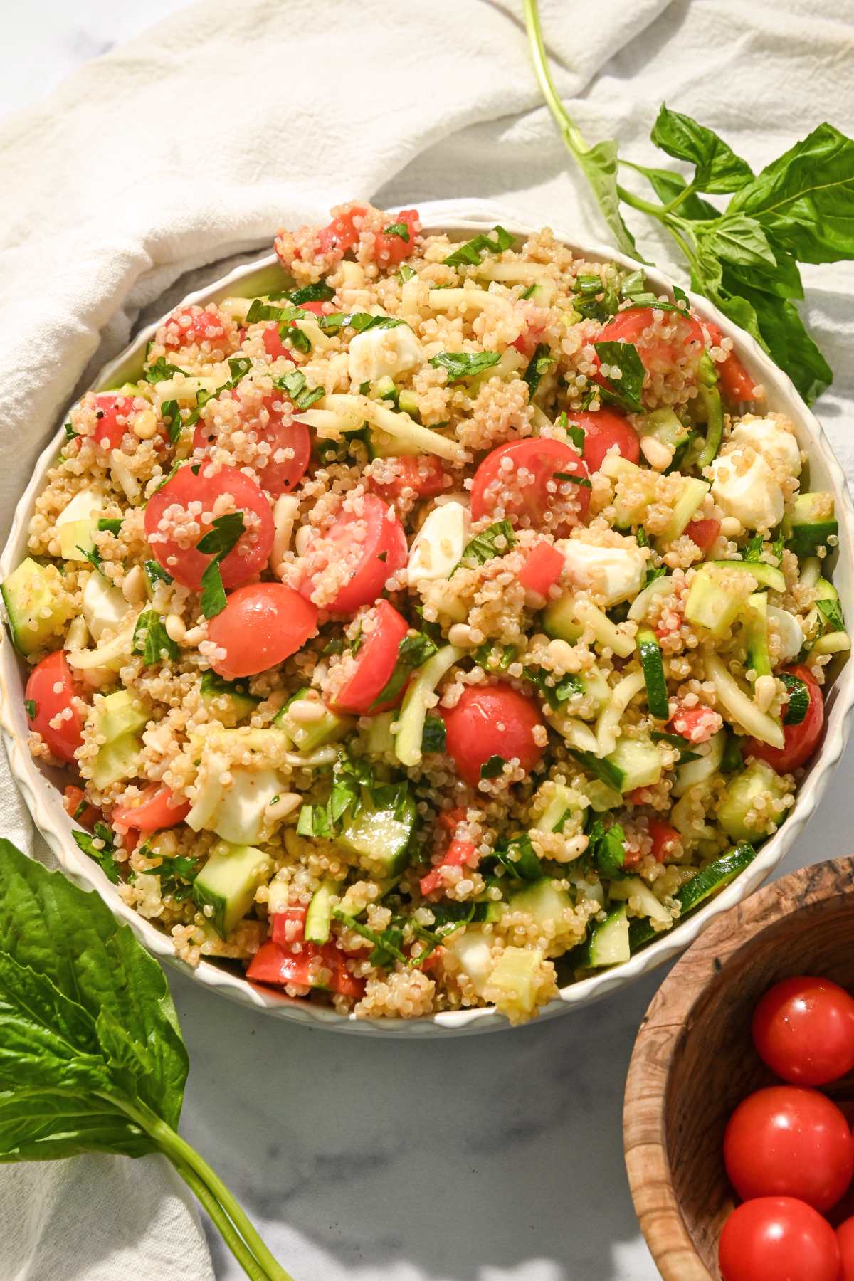 full view of Italian caprese quinoa salad in a white bowl with salad ingredients around it.