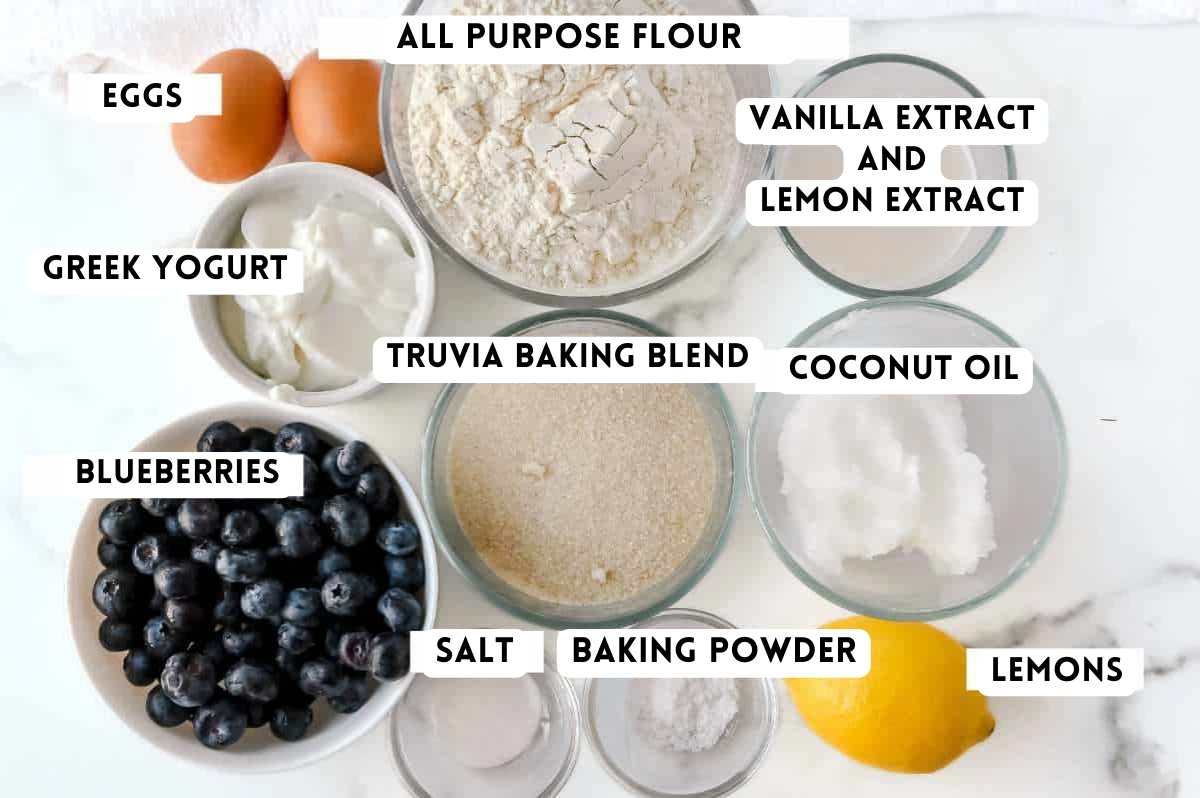 labeled blueberry lemon cake ingredients on a white marble background.