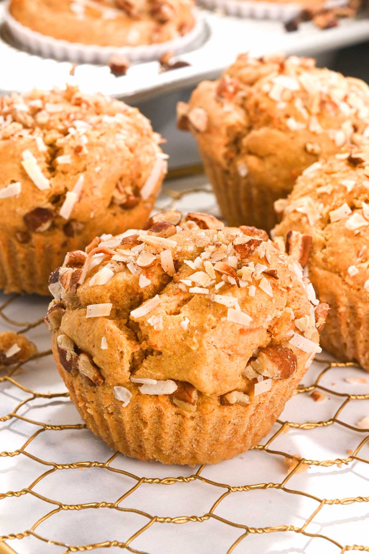 carrot cake protein muffin on a cooling rack with muffins behind in a tin.